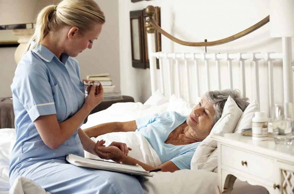 A palliative care worker checking on a senior lady in her bed